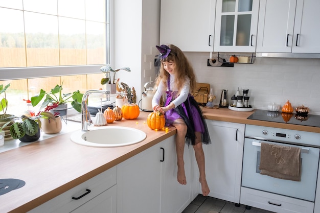 Kind versiert de keuken in huis voor Halloween Meisje in een heksenkostuum speelt met het decor voor de vakantie vleermuizen jack lantaarn pompoenen Herfst comfort in huis Scandistyle keuken loft