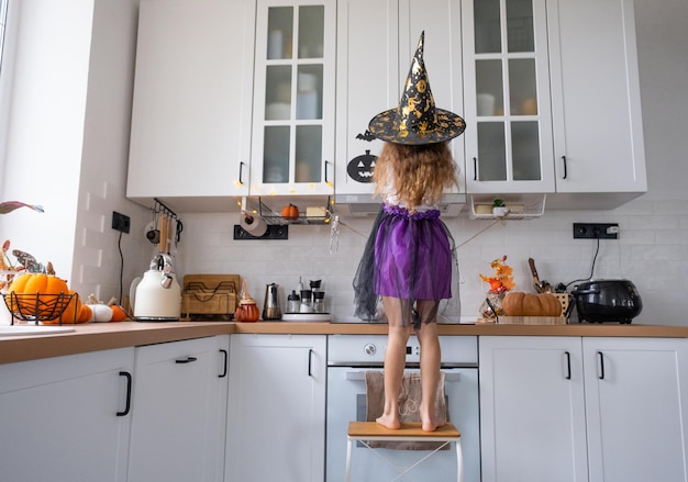 Kind versiert de keuken in huis voor Halloween Meisje in een heksenkostuum speelt met het decor voor de vakantie vleermuizen jack lantaarn pompoenen Herfst comfort in huis Scandistyle keuken loft