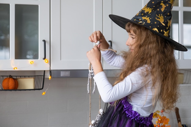 Kind versiert de keuken in huis voor Halloween Meisje in een heksenkostuum speelt met het decor voor de vakantie vleermuizen jack lantaarn pompoenen Herfst comfort in huis Scandistyle keuken loft