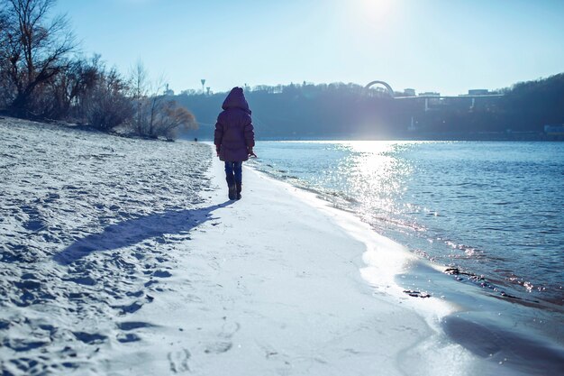 Kind wandelen langs de oever van de rivier en genieten van zonnige winterdag