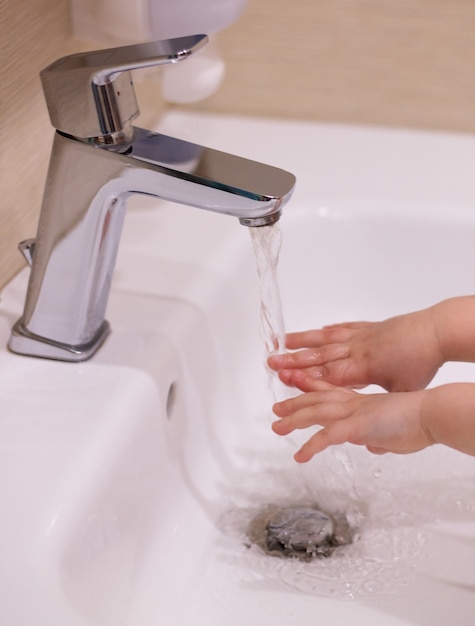 Kind wast handen. Klein meisje wast haar handen met zeep onder een kraan met stromend water. Detailopname. Hygiëne, schoon en gezondheidsconcept