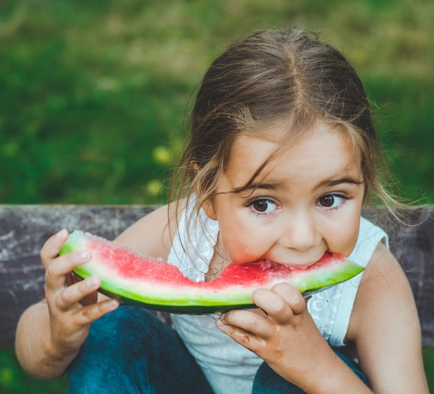 Kind watermeloen eten in de tuin. Kinderen eten fruit buitenshuis. Gezonde snack voor kinderen. Klein meisje spelen in de tuin bijten een plakje watermeloen.