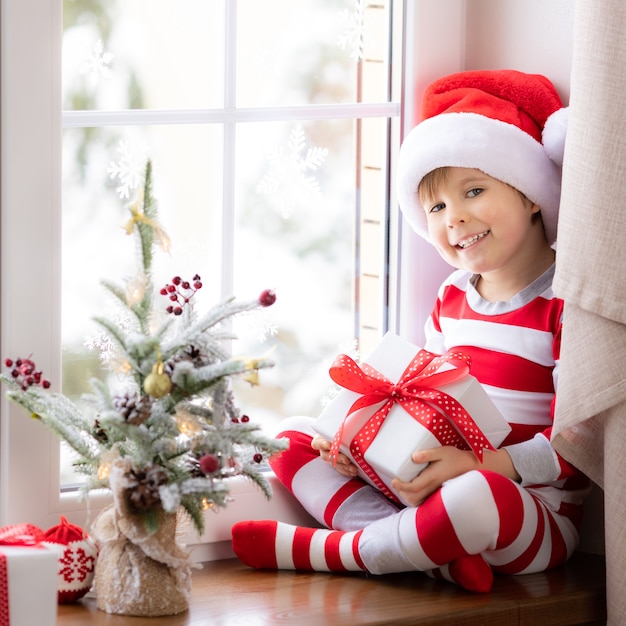 Kind zit op vensterbank Gelukkig kind draagt kerstpyjama