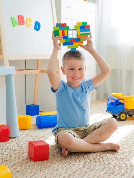 Kind zit vloer kamer spelen. Heldere bouwstenen vormen harthanden van kinderen.