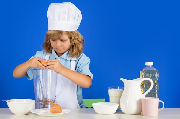 Kindchef-kok bereidt voedsel in geïsoleerde blauwe studio-achtergrond, kinderen koken tienerjongen met schort en