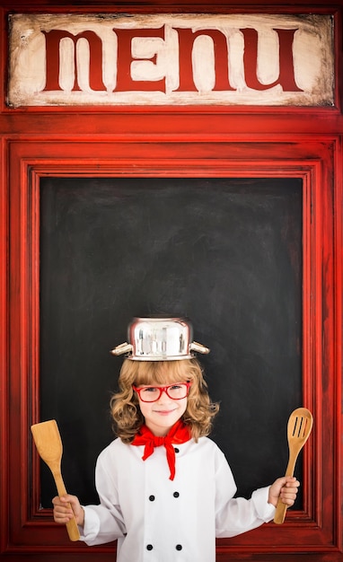 Foto kindchef-kok tegen leeg bordmenu met het tekenen van gezond voedsel restaurant bedrijfsconcept