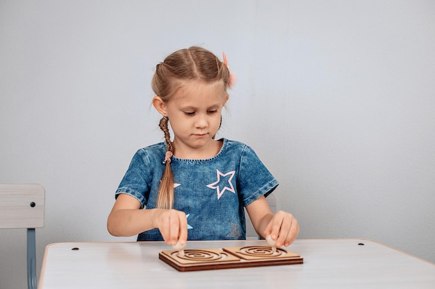 Kinder ontwikkeling. Jonge, heldere, gefocuste vrouwelijke jongen die aan tafel zit en de puzzel voor hersenontwikkeling oplost. Vooruitgangsconcept. foto met ruis