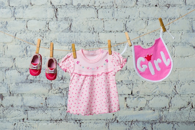 Foto kinder slabbetje jurk en rode schoenen voor het meisje droog aan een touw op een witte bakstenen muur