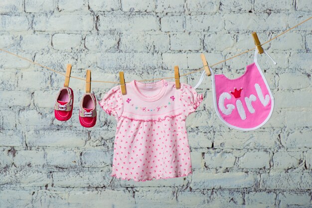 Kinder slabbetje jurk en rode schoenen voor het meisje droog aan een touw op een witte bakstenen muur