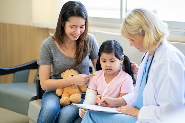 Kinderarts arts die een klein Aziatisch meisje onderzoekt met een gebroken arm die een gipsverband draagt in het ziekenhuis