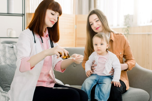 Kinderarts het geven van een siroop voor zieke babymeisje, zittend met moeder en toont de dosering