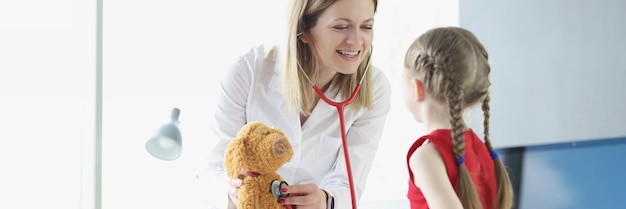 Foto kinderarts laat klein meisje zien hoe ze een stethoscoop moet gebruiken met speelgoed als voorbeeld kinderarts