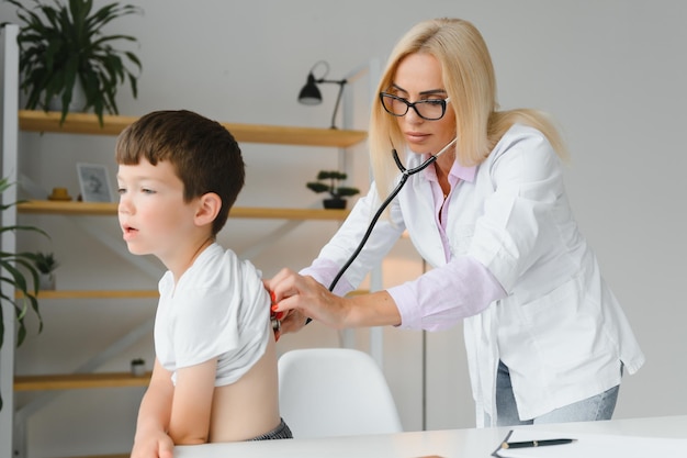 Kinderarts luistert naar ademen in de longen en hartslag met een stethoscoop Portret van een schattige kleine jongen die een dokter bezoekt