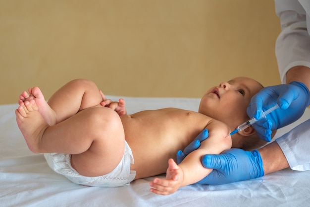 Foto kinderarts vaccin geven aan baby liggend op zijn rug.