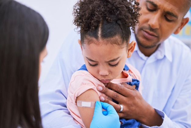 Kinderarts vader en meisje met gips voor vaccin griepprik of medicijninjectie in kliniek of ziekenhuis Vader kind met verband en arts op kantoor voor vaccinatieconsultatie en kinderopvang