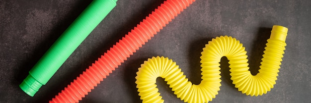 Foto kinderen anti-stress sensorische pop buis plastic fidget duw speelgoed op een zwarte tafel of vloer achtergrond. kinder poptube speelgoed multicolor hue felle kleur. spandoek. bovenaanzicht, plat gelegd