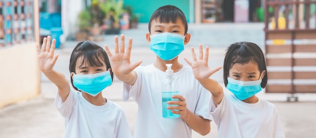 Kinderen die een masker dragen en alcoholgel vasthouden om het coronavirus te doden en hun hand niet naar huis te laten gaan