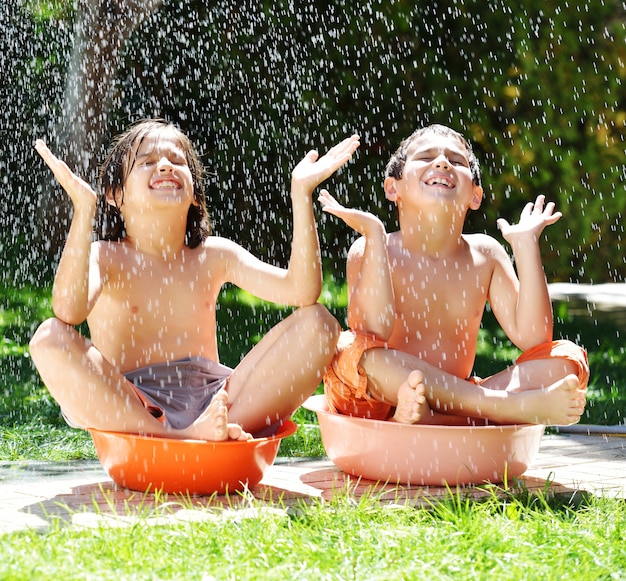 Kinderen die en met watersproeier spelen bespatten op de zomergraswerf