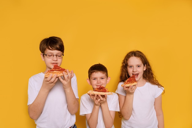 Kinderen die pepperony pizza op gele muur eten.