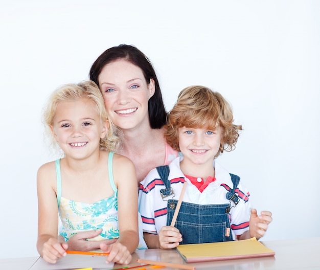 Kinderen die thuiswerk met hun moeder doen die bij de camera glimlachen