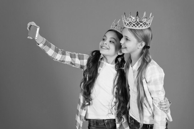 Kinderen dragen gouden kronen symbool prinses waarschuwingssignalen van verwend kind vermijd het opvoeden van verwende kinderen meisjes nemen selfie foto smartphone camera verwend kinderconcept vraag meer aandacht