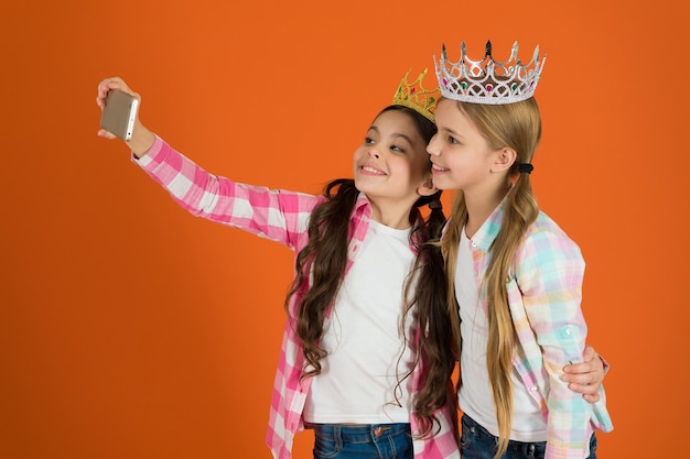 Kinderen dragen gouden kronen symbool prinses Waarschuwingssignalen van verwend kind Vermijd het opvoeden van verwende kinderen Meisjes nemen selfie foto smartphone camera Verwend kinderconcept Vraag meer aandacht