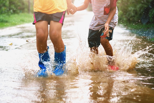 kinderen dragen regenlaarzen en springen in plas op regenachtige dag