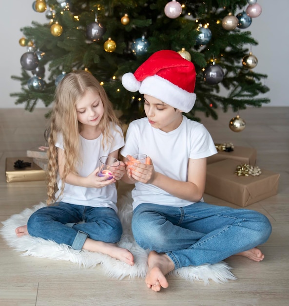 Kinderen - een jongen en een meisje spelen in de buurt van de kerstboom. Woonkamer interieur met kerstboom en versieringen. Nieuwjaar. Cadeaus geven.