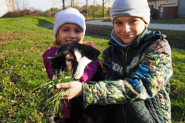 Kinderen een jongen en een meisje van blank ras lopen een zwart-witte kat op het grasveld bij het huis De kat is bang voor een nieuwe plek en probeert uit de hand te lopen Herfst zonnige dag