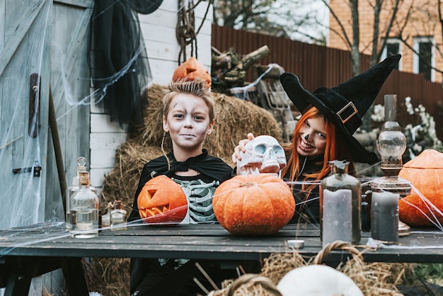 Foto kinderen een jongen in een skeletkostuum en een meisje in een heksenkostuum die plezier hebben op een halloweenfeest op de versierde veranda