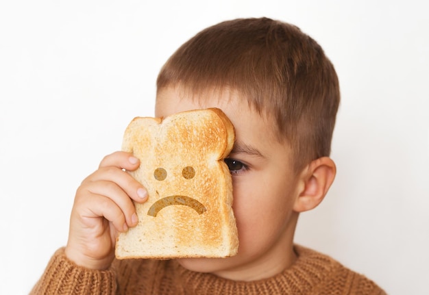 Kinderen en gluten. Peuterjongen met geroosterd brood, met droevige emoji. Glutenintolerantie bij kinderen.