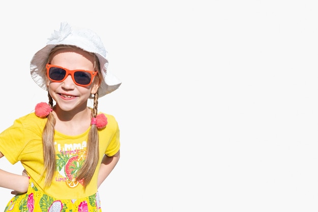 Kinderen en zomer Een gelukkig emotioneel klein meisje met een hoed, zonnebril en een gele jurk lacht en glimlacht