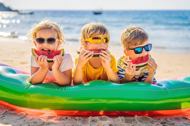 Kinderen eten watermeloen op het strand in zonnebril