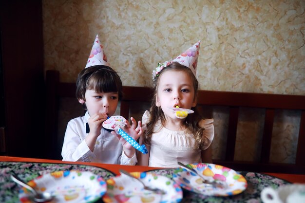 Kinderen feest in caps verjaardag vieren met taart en ballonnen thuis.