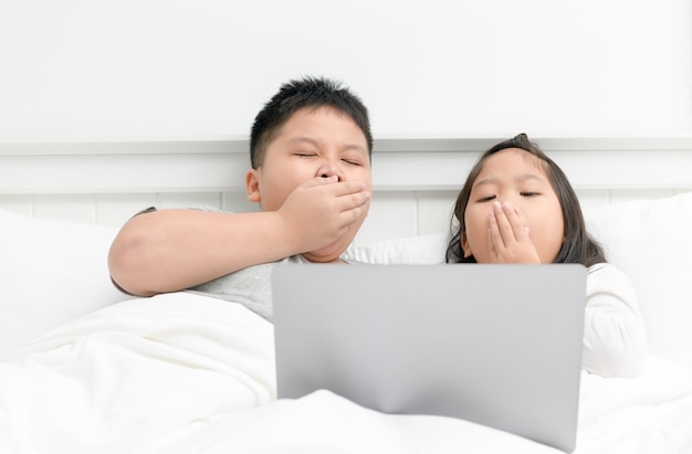 Kinderen gapen en spelen computer op bed