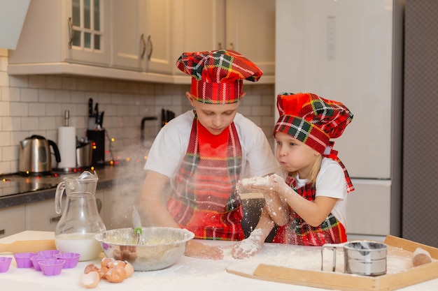 Kinderen in chef-kokkostuums bereiden deeg van meel-melkeieren voor kerstgebakjes