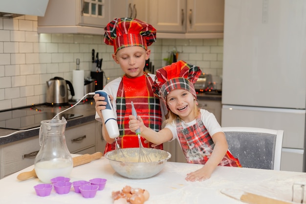 Kinderen in chef-kokkostuums bereiden deeg van meel-melkeieren voor kerstgebakjes