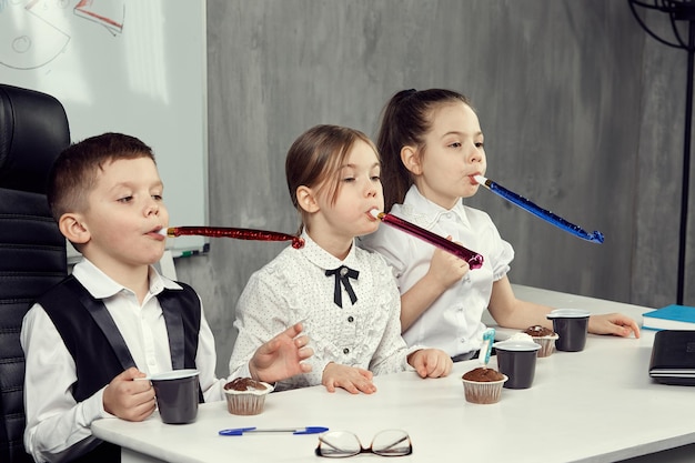 Kinderen in de beelden van kantoorpersoneel blazen pijpen op een feestdag op kantoor