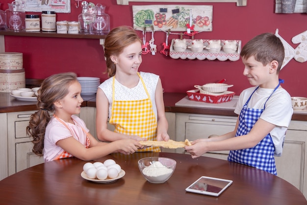 Kinderen in de keuken proberen te leren koken. Beste vrienden in schorten die gebak in hun handen houden en cake maken in de keuken en naar elkaar kijken. Studio opname.