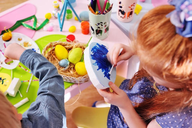 Kinderen in de kleuterschool schilderen eieren voor de paasmand aan de tafel.