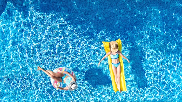 Kinderen in de luchtfoto van het zwembad vanuit de drone, gelukkige kinderen zwemmen op opblaasbare ringdonut en matras, actieve meisjes hebben plezier in het water tijdens een familievakantie op vakantieoord