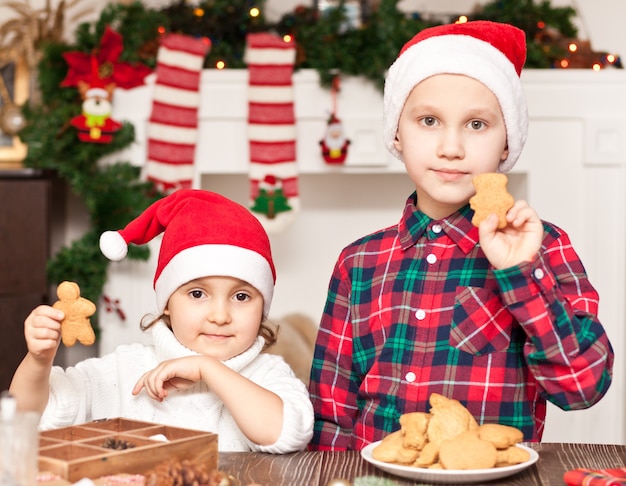 Kinderen in een kerstmuts met kerstkoekjes thuis.