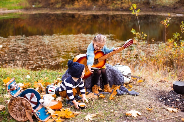 Kinderen in het herfstbos op een picknickgrill worstjes en gitaar spelen