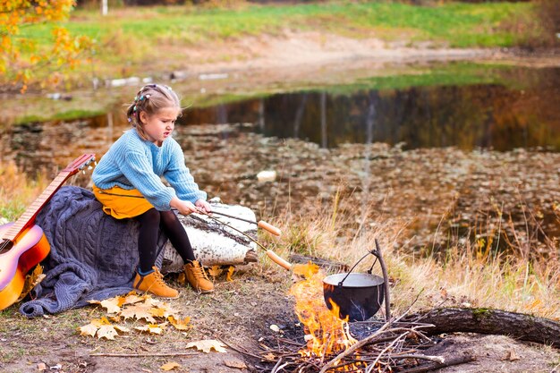 kinderen in het herfstbos op een picknickgrill worstjes en gitaar spelen