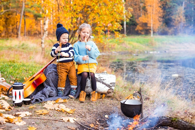 kinderen in het herfstbos op een picknickgrill worstjes en gitaar spelen