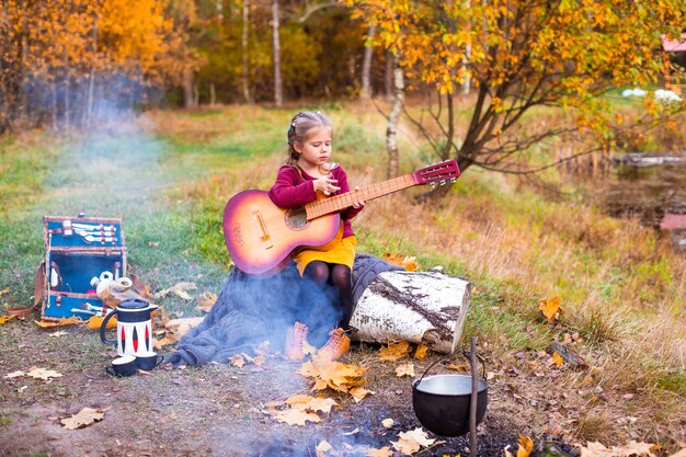 kinderen in het herfstbos op een picknickgrill worstjes en gitaar spelen