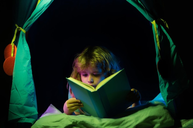 Kinderen in kindertent die een boek lezen in het donkere huis kindjongen die een boek leest liggend op het bed dromend