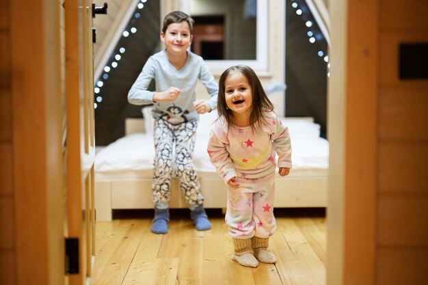 Kinderen in zachte, warme pyjama's die in een houten hut thuis spelen. Concept van geluk in de kindertijd. Broer en zus hebben plezier en spelen samen