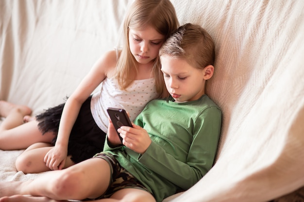 Foto kinderen kijken naar video's over gadgets die op de bank liggen