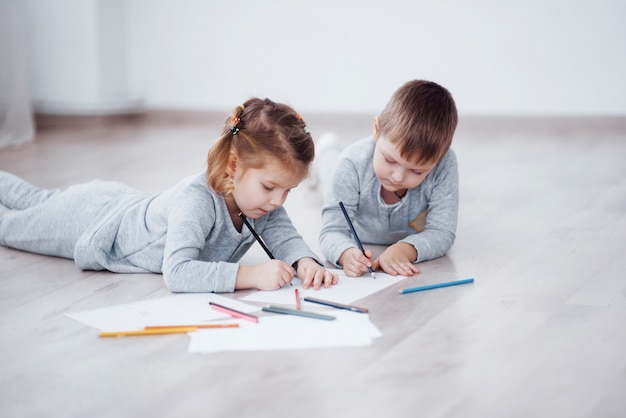 Kinderen liggen op de vloer in pyjama en tekenen met potloden. Schattig kind schilderij van potloden